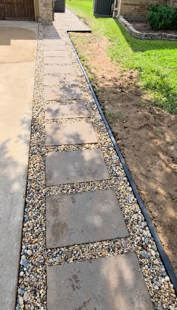 Side yard river rock extension with stepping stones running alongside a driveway