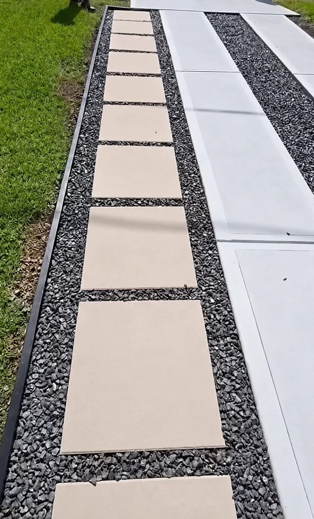 Square stepping stones set in gravel beside a concrete driveway to widen the parking edge